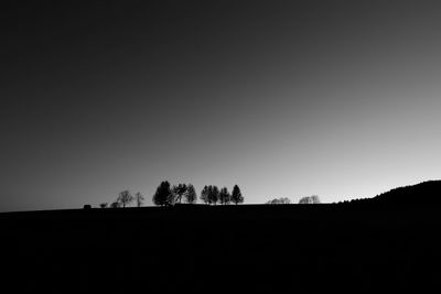 Silhouette trees on field against clear sky