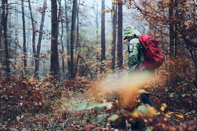 Woman with backpack wandering around a forest on autumn cold day