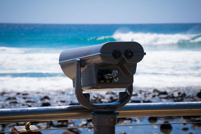Close-up of coin-operated binoculars by sea against sky