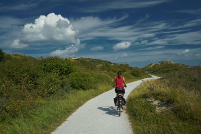 Woman riding bicycle on road against sky