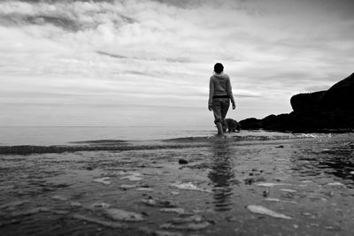 Rear view of man standing at beach against sky