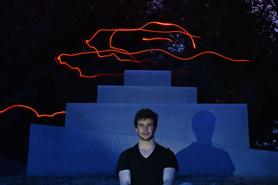 Young man sitting against light painting at night