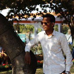 Young man wearing sunglasses standing against trees