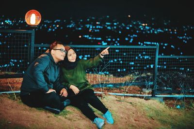 Young couple sitting on illuminated street at night