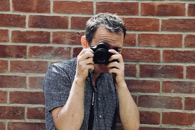 Portrait of man photographing against brick wall