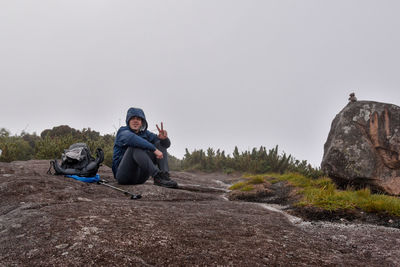 Man sitting on rock against sky