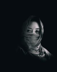 Portrait of young woman wearing scarf against black background