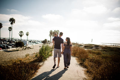 Parents holding hands walking alongside sand dunes with son