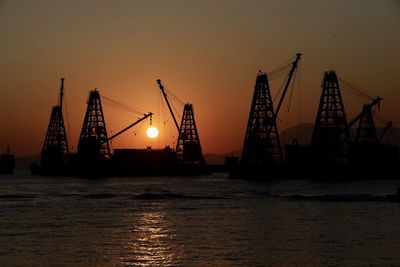 Silhouette cranes at commercial dock against sky during sunset