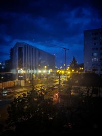 Illuminated buildings by street against sky at night