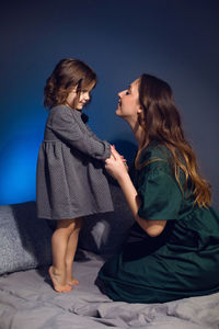 Mother and daughter in dresses sitting on a bed in a bedroom with a blue wall