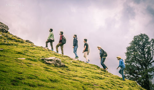 Low angle view of people standing on mountain against sky