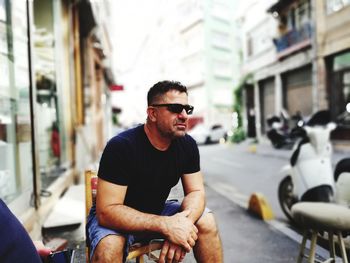 Man in sunglasses sitting on sidewalk 