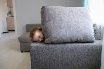 Kid toddler builds house from pillows on sofa in living room, lifestyle and games in real interior
