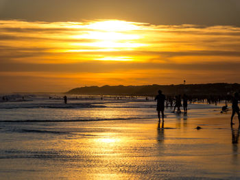 Silhouette people walking on beach against sky during sunset