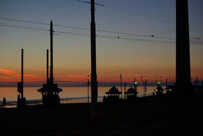 Silhouette of electricity pylons against sky during sunset