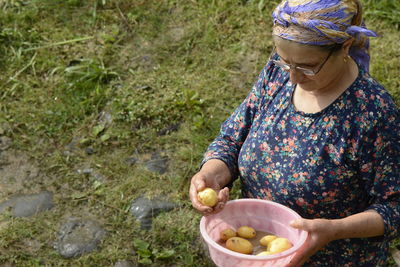 Woman holding potatoes in container on field