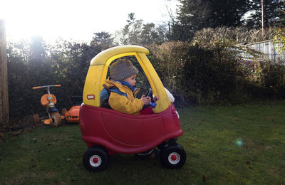 Girl driving toy car on grassy field in backyard