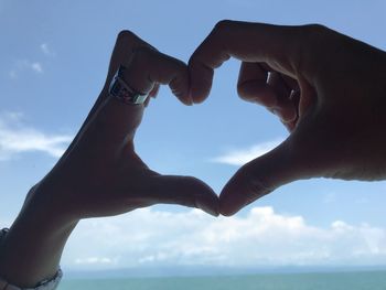 Close-up of hand against sky over sea