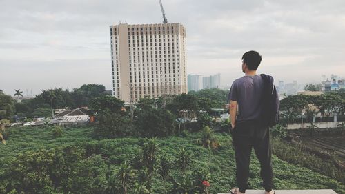 Rear view of man standing by buildings against sky