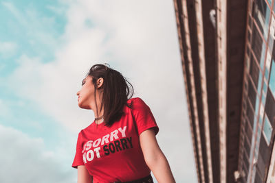 Young woman looking away while standing against sky