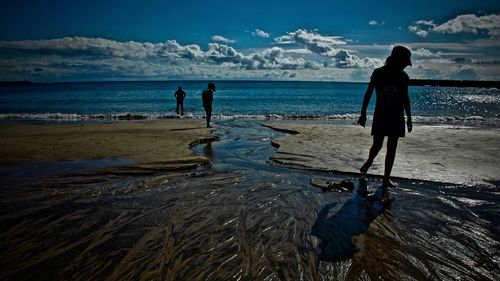 Silhouette people walking on calm beach