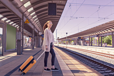 Young woman with luggage standing at railroad station