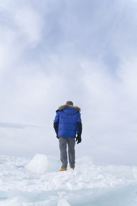 Rear view of man walking on snow against sky