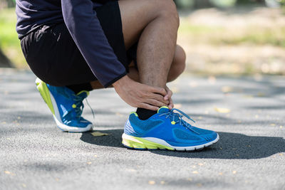 Low section of man touching ankle in pain on road