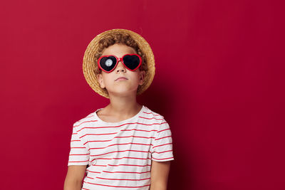 Boy wearing hat and sunglasses against red background
