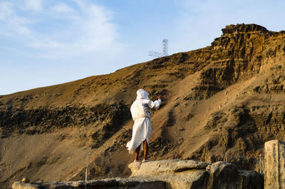 Rear view of man on rock against sky