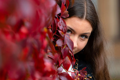 Close-up portrait woman peeking near red plant