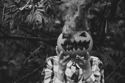 Close-up of woman hand holding smoke emitting jack o lantern outdoors