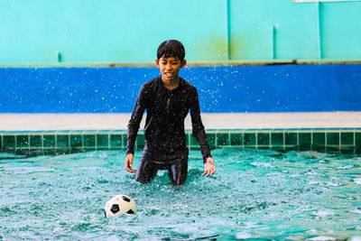 Full length of boy playing with ball in swimming pool