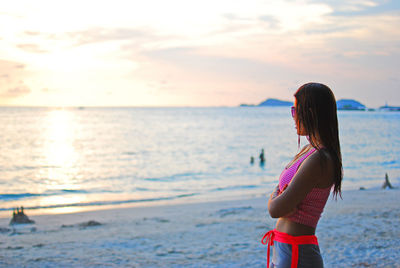 Side view of mid adult woman looking at sea against sky during sunset