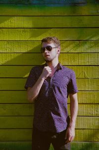 Young man wearing sunglasses standing against wall