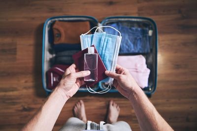 Preparing for travel in new normal. man packing passport, face masks and hand sanitizer.