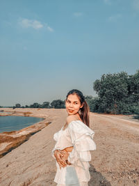 Portrait of smiling young woman standing on land against sky