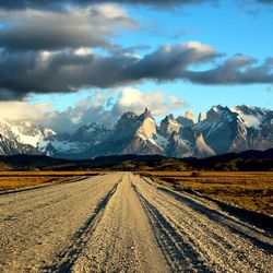 Dirt road leading towards snow covered mountains against sky