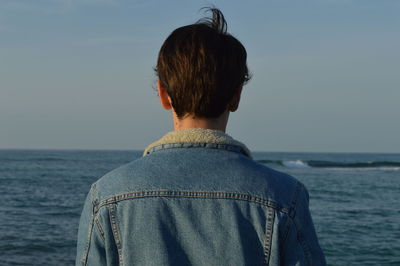 Rear view of man standing by sea against clear sky during sunset