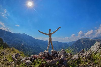 Wooden figurine on mountain against sky during sunny day