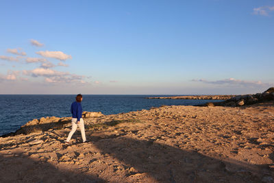 Full length of woman walking by cliff against sea and sky