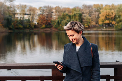 A woman in a city park by the river uses a smartphone