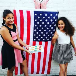 Portrait of siblings holding muffins while standing by american flag smiling young woman
