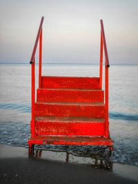 Red deck chairs on beach against sky