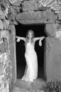 Sad young woman wearing white dress standing on doorway