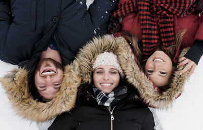 High angle portrait of smiling friends lying on snow covered field