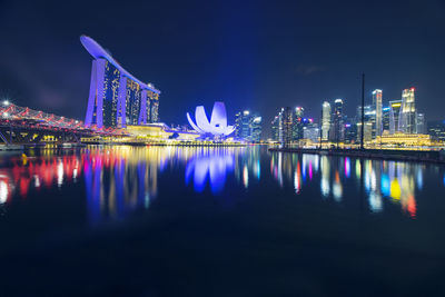 Illuminated buildings by river against sky at night