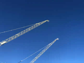 Low angle view of cranes against clear blue sky