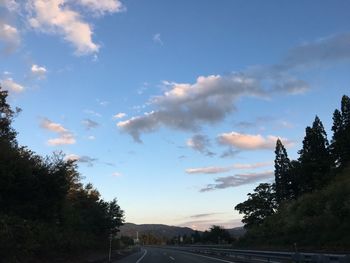 Country road by trees against sky